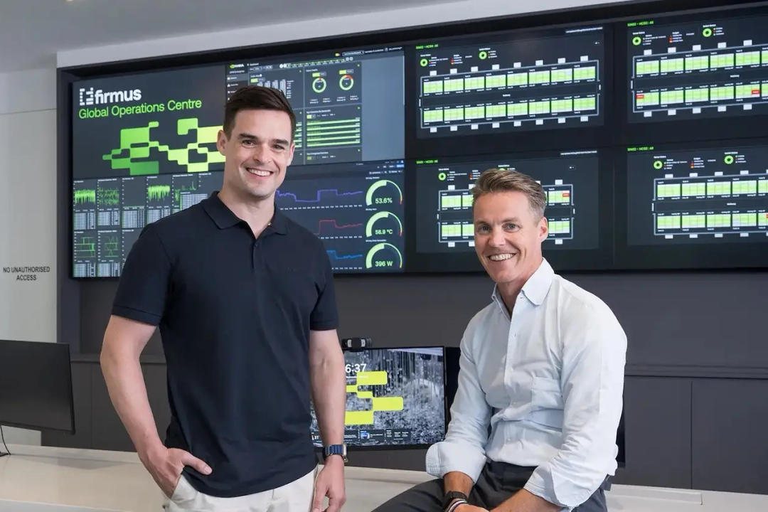 Two men standing in front of monitoring screens at Firmus Global Operations Centre, displaying dashboards with green indicators.