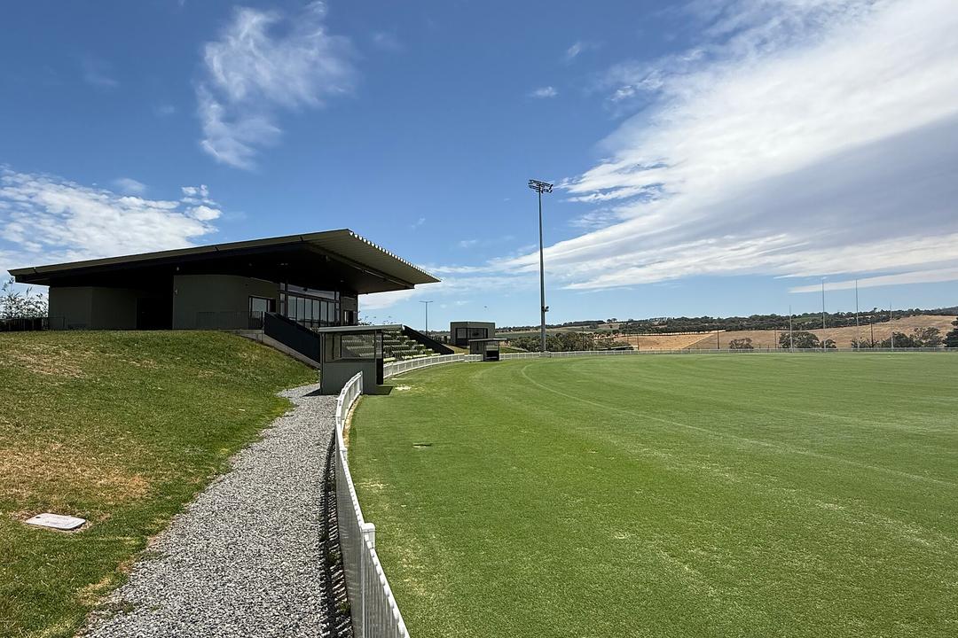 Modern black pavilion with manicured green field, floodlight, white fence, rolling rural landscape