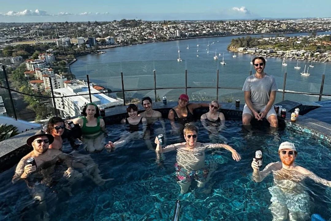 Group enjoying rooftop infinity pool overlooking coastal harbour on sunny day