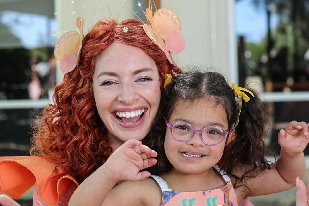Woman with red curly hair and child in purple glasses, both smiling, wearing festive hair decorations