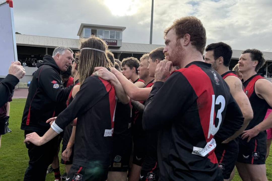 Australian rules football team in black and red with coach after victory