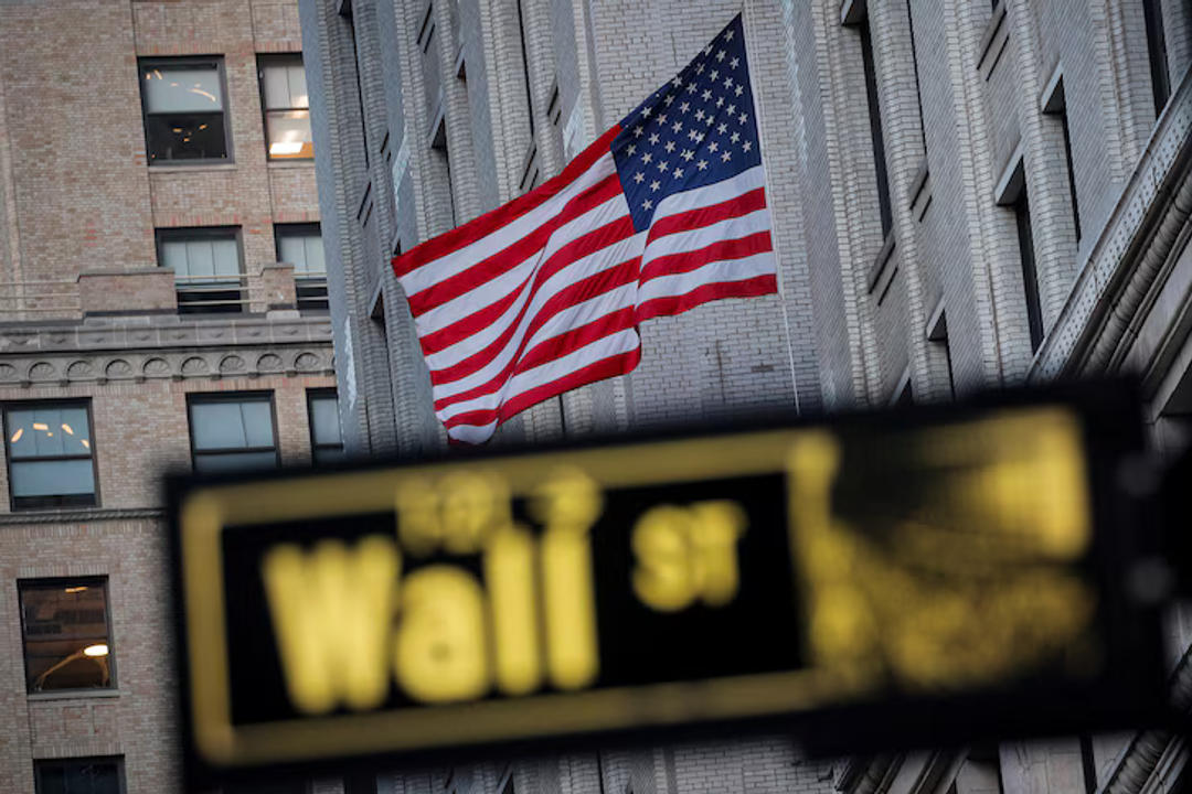 American flag flying in front of brick buildings with blurred street sign in foreground