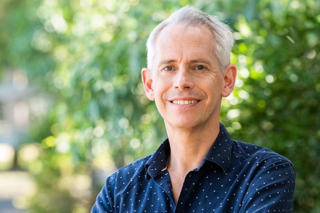 Andrew Giles. Middle-aged man with grey hair in navy dotted shirt against blurred garden background