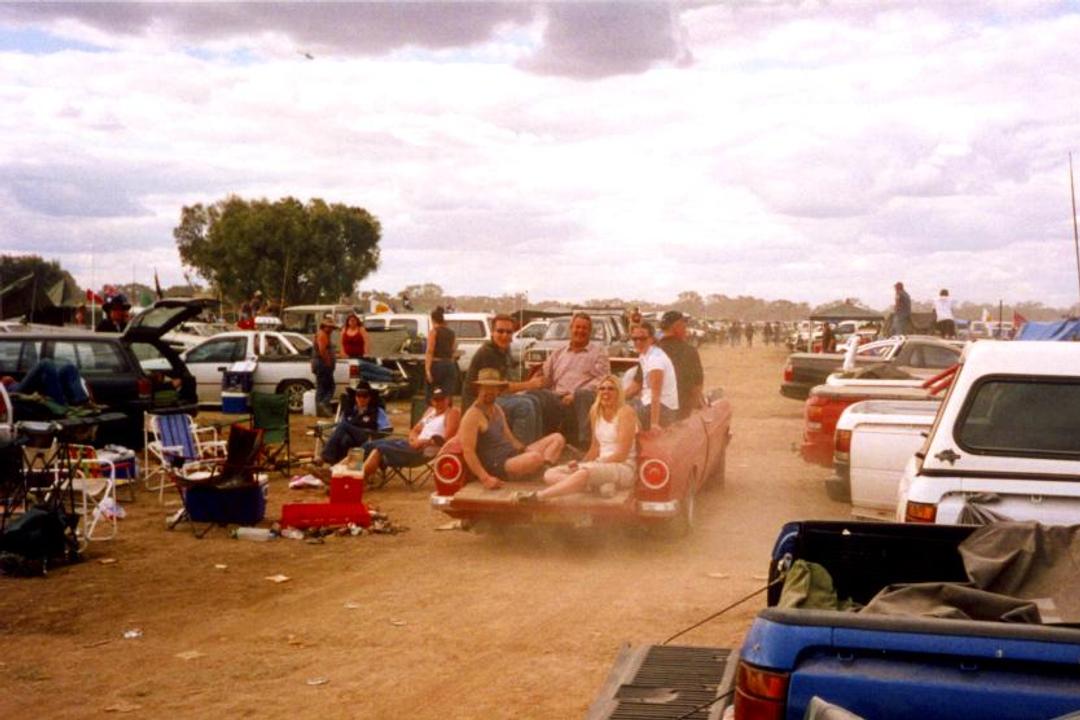 File image: Large outdoor gathering with parked vehicles and crowds of people at dusty rural event.