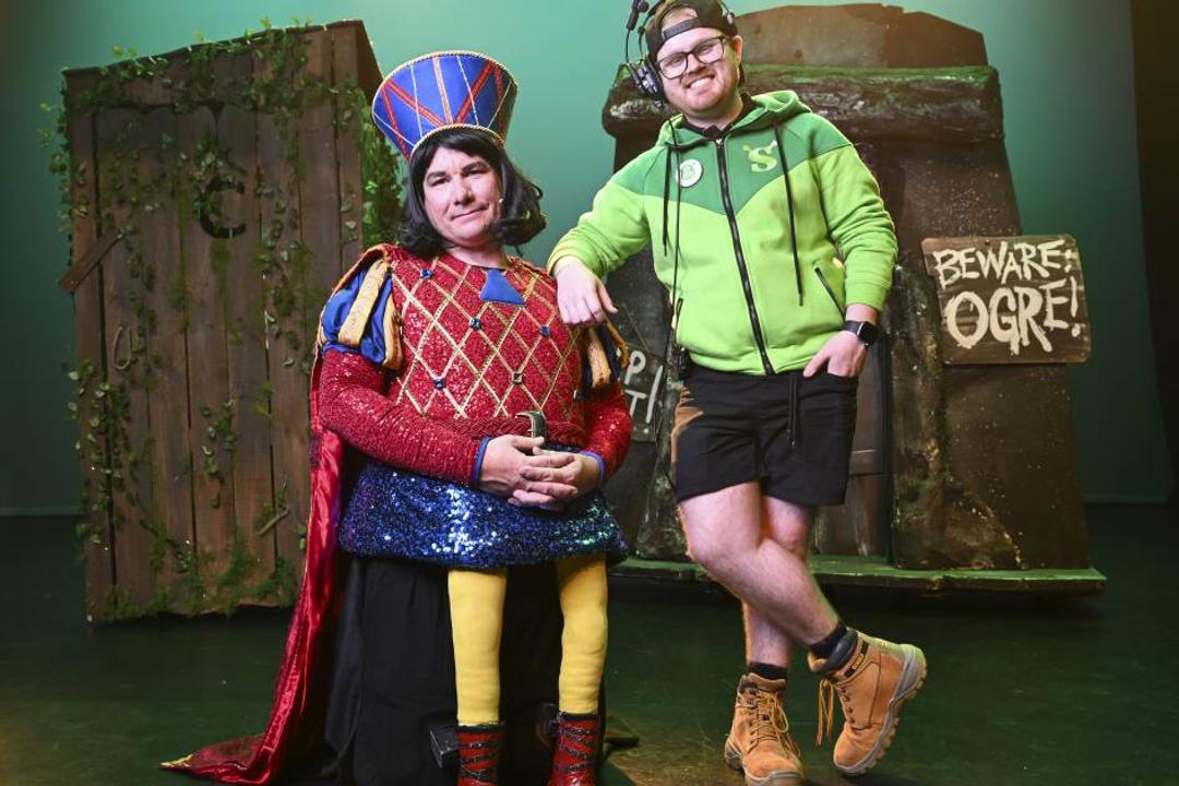 Two people in theatrical costumes posed before set with 'Beware Ogre' sign