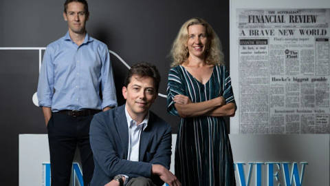 Three professional people posed against dark background with Australian Financial Review newspaper behind them