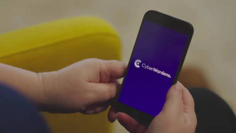 Person holding smartphone displaying CyberWardens logo on purple screen