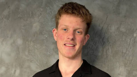 Ben Adler. Professional headshot of young person with curly brown hair smiling against textured gray background