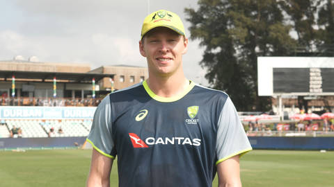 Australian cricketer in Qantas team uniform on cricket ground, smiling at camera