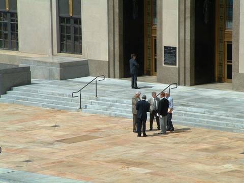 File image: Modern institutional building courtyard with steps and figures in business attire, formal legal setting.