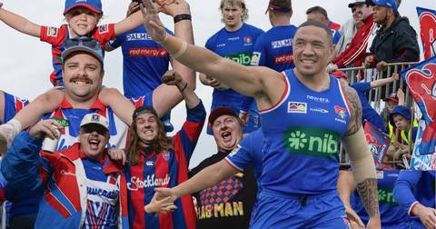 Newcastle Knights fans and players celebrating outdoors, group includes child on adult's shoulders, all wearing team jerseys