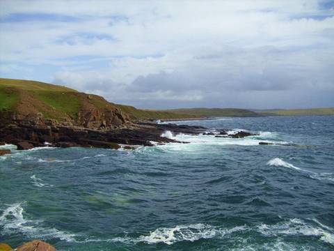 File image: Rocky coastline with crashing waves, green cliffs, cloudy sky