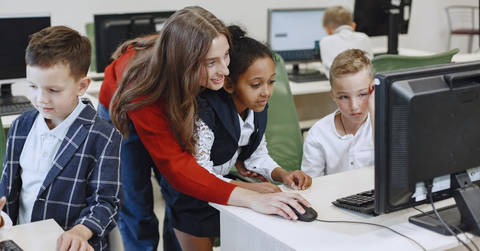 File image: Teacher and students gathered around a desktop computer in a classroom technology lab.