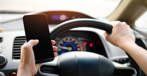 File image: Driver holding phone with one hand on steering wheel inside moving car
