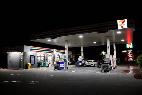 File image: 7-Eleven style service station lit at night with fuel pumps and convenience store.