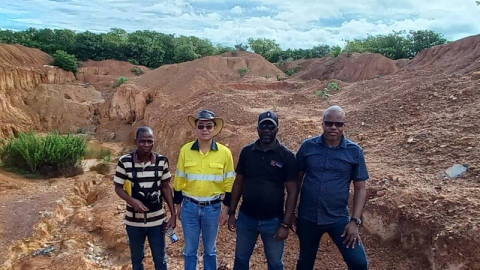 Four men standing at open-pit mining site with tropical landscape and earth mounds