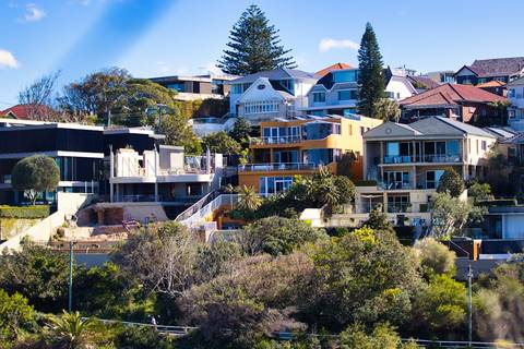 File image: Hillside suburban houses among trees under blue sky