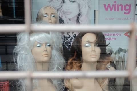File image: Storefront window displaying mannequin heads wearing wigs with 'wing extension system' signage visible.