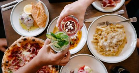 Overhead restaurant scene with plated dishes, cocktails and diner's hands at table