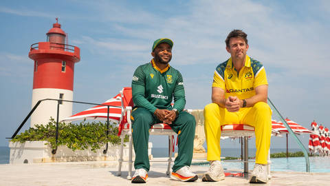 Two cricket players in South Africa and Australia uniforms seated by a poolside with a red and white striped lighthouse behind them