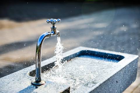 Water stream flowing from metal tap into basin outdoors