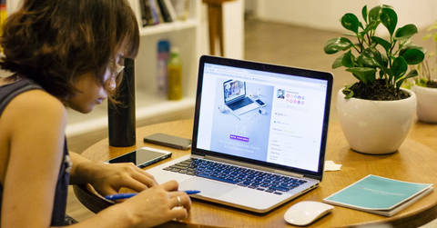 Woman working at laptop desk with plant, representing home office work environment.