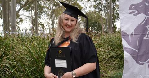 Luba Makarov. Woman in graduation gown holding University of Newcastle diploma, outdoors