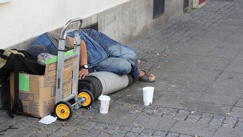 Person on street with cardboard box and belongings illustrating homelessness context