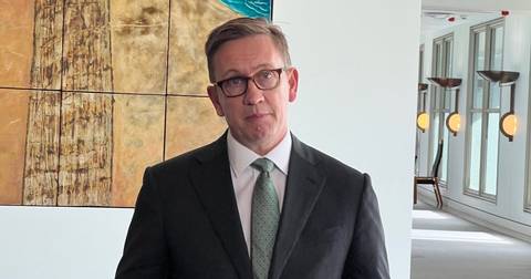 Man in dark suit and glasses, professional indoor setting with artwork background