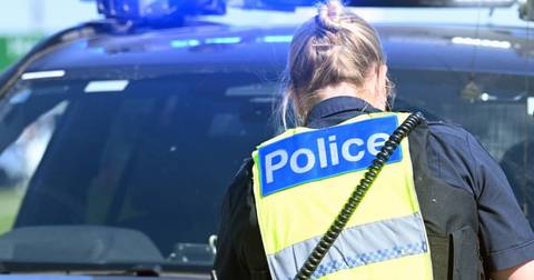 Police officer from behind in high-visibility vest standing near police vehicle