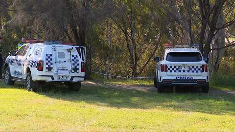 Two white Australian police vans parked on grass beside trees