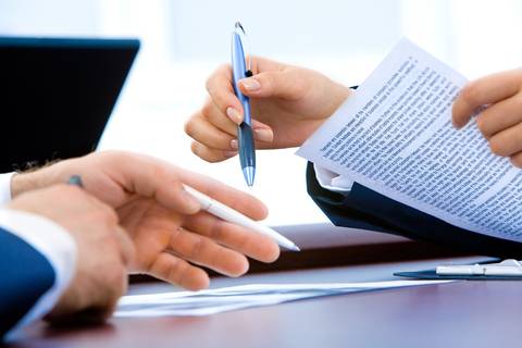 File image: Person pointing at document text while colleague reviews contract or financial paperwork