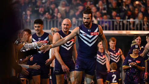 Fremantle AFL players in navy jerseys interact with supporters during a match