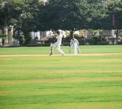 Batsman in white clothing striking ball at crease during professional cricket match on well-maintained field.