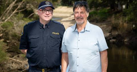 Police officer in uniform standing with older man in light shirt against rural background