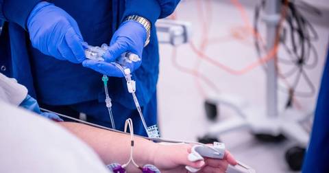 Medical professional in blue gloves administering IV line to patient's arm in hospital
