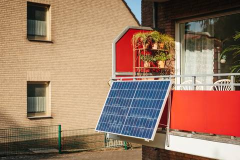 Solar panel mounted on red-framed apartment balcony with brick building facade