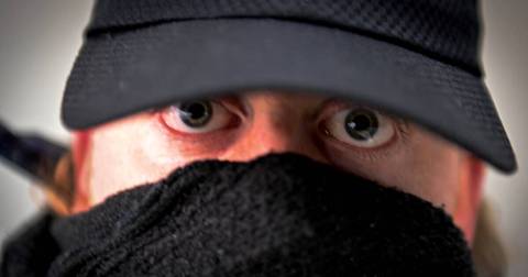 Close-up of person wearing dark cap and black scarf covering lower face.