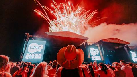 Crowd at CMC Rocks concert with fireworks, stage, red cowboy hat, and CMC branded screens