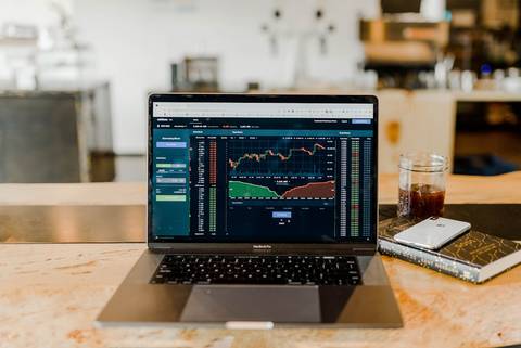 File image: Person at wooden desk with laptop displaying financial charts and trading data, coffee nearby