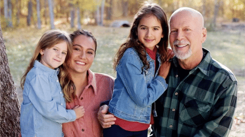 Family of four posing outdoors smiling at camera in casual clothing
