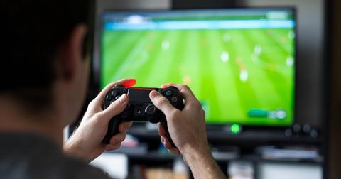 Person holding PlayStation controller playing game on TV screen indoors