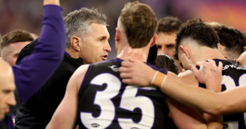 Justin Longmuir. Coach in black jacket instructs players wearing purple and black football uniforms during game