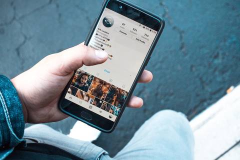 File image: Hand holding phone displaying Instagram profile with follower counts and photo grid