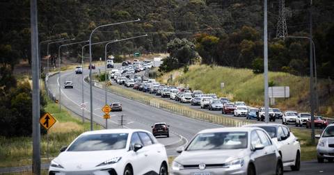 Multiple vehicles lined up on Australian highway with trees, street lights, and power transmission tower