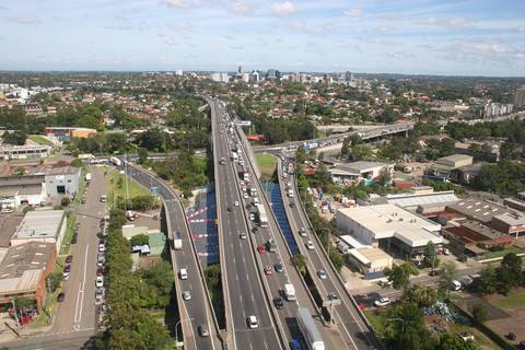 File image: Aerial view of multi-lane motorway with traffic through suburban landscape with city skyline.