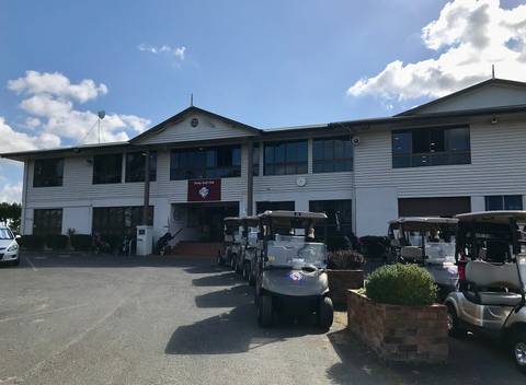White golf clubhouse with windows and parked golf carts in front.