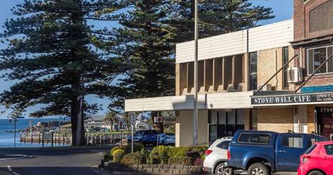 Street-level view of Stone Wall Cafe and neighboring shops with parked vehicles and trees