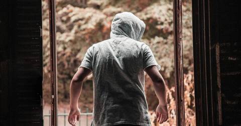 Person from behind in gray t-shirt and hood near brick building and metal railing