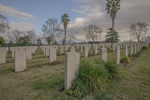 File image: Wide view of military cemetery with rows of white headstones, trees, and cloudy sky